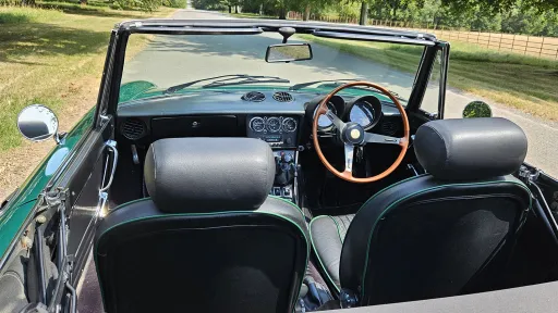 View through the open roof of green Alfa Romeo Spider Veloce showing black leather interior and wooden steering wheel.