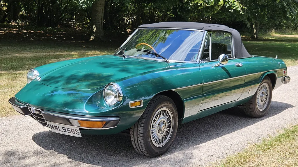 Front left view of dark racing green Alfa Romeo Spider Veloce with black soft top roof raised.