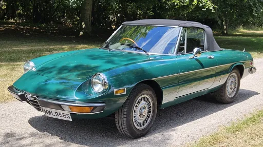 Front left view of dark racing green Alfa Romeo Spider Veloce with black soft top roof raised.