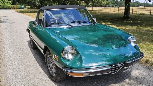 Front right view of dark racing green Alfa Romeo Spider Veloce with black soft top roof closed.