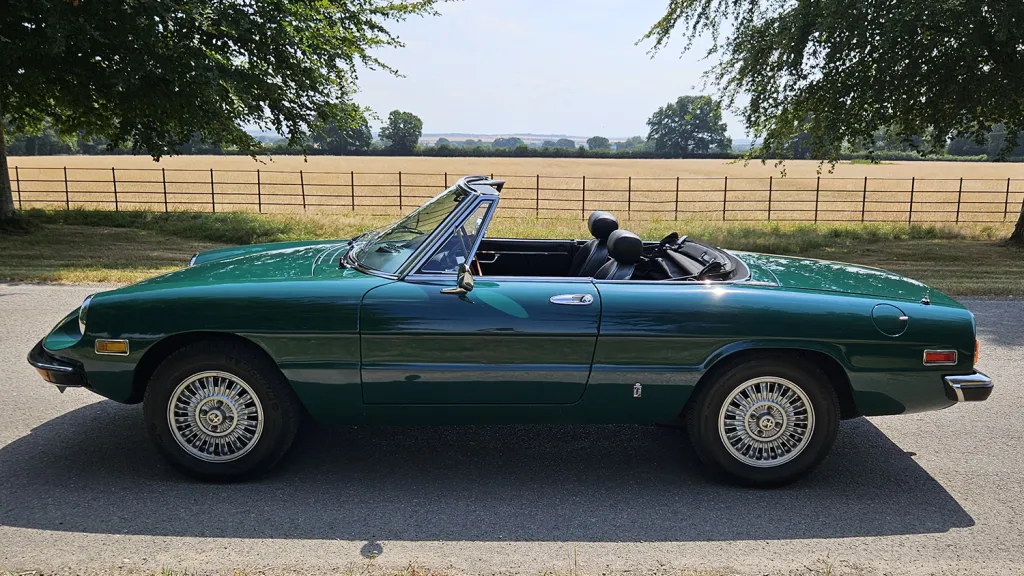 Full left side profile of dark racing green Alfa Romeo Spider Veloce convertible with open roof.