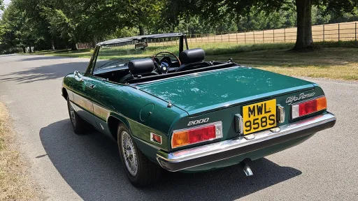 Rear left view of dark racing green Alfa Romeo Spider Veloce with black soft top folded down.