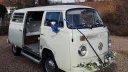 Front view of white 1974 Volkswagen Bay Window campervan decorated with blue wedding ribbons and flowers.