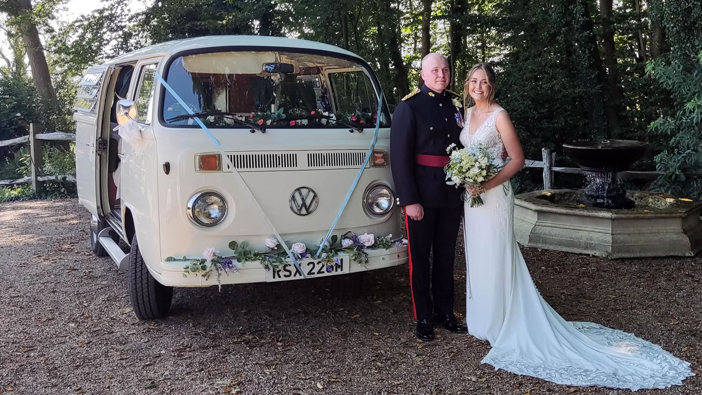 Bride and groom standing beside white 1974 VW Bay Window campervan at an Essex wedding venue.