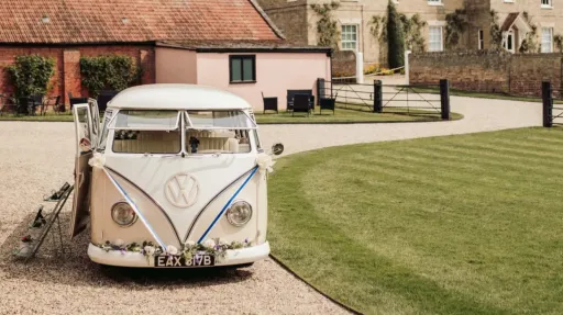 Front view of cream and beige 1964 VW Split Screen Campervan with safari windows parked outside an Essex wedding venue.