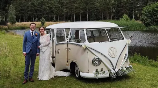 Bride and groom standing beside cream and beige 1964 VW Split Screen Campervan decorated with wedding flowers in Essex.