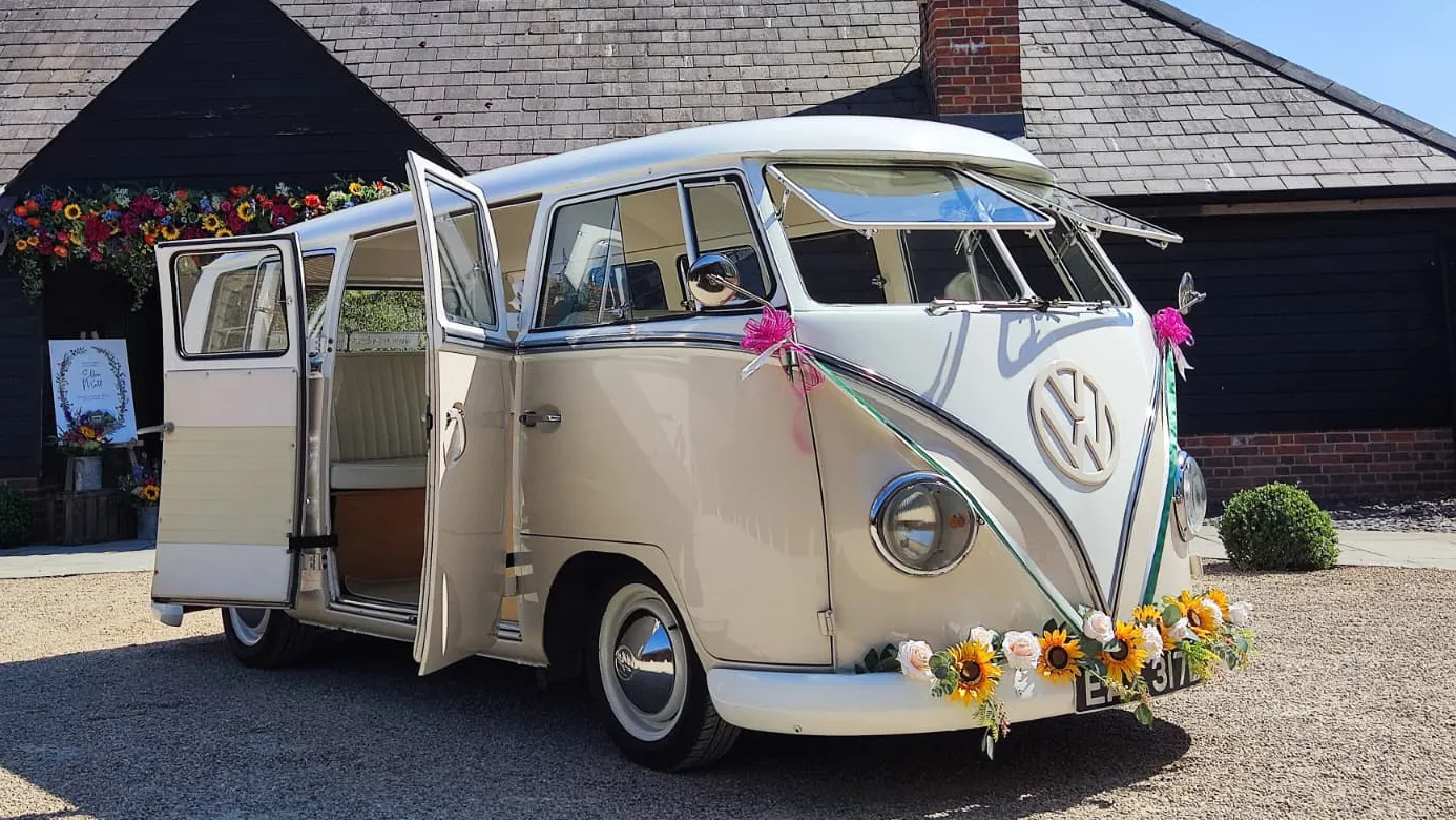 Front three quarter view of cream and beige 1964 VW Split Screen Campervan with opening safari windows and wedding decorations.
