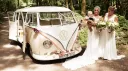 Two brides standing beside cream and beige 1964 VW Split Screen Campervan decorated with flowers for their wedding.