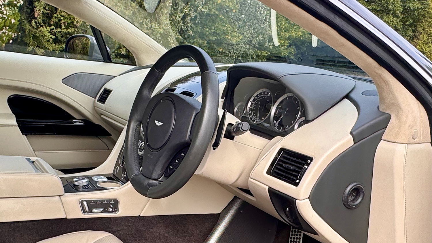 Driver side interior of Aston Martin Rapide S with cream leather seats, dashboard and centre console.