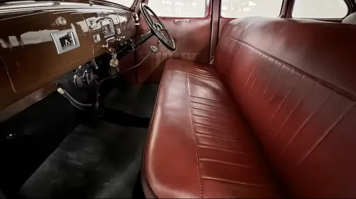 Front cabin of 1937 Hudson Terraplane showing maroon red leather bench seat, period dashboard and steering wheel.