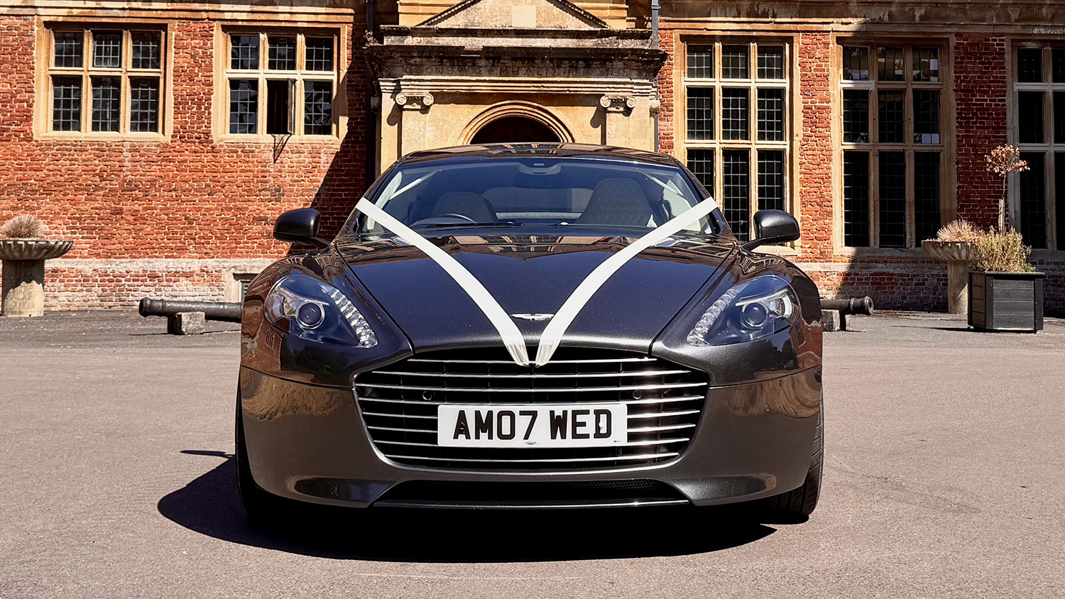 Front view of metallic silver Aston Martin Rapide S decorated with traditional white wedding ribbons.