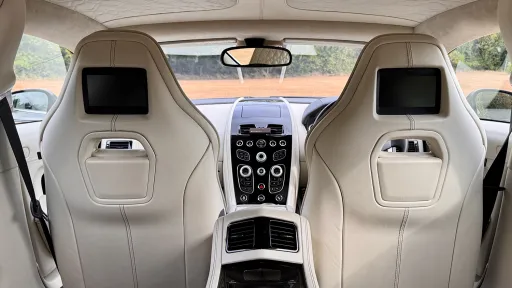 View from the rear cabin of Aston Martin Rapide S showing cream leather front seats with integrated screens and centre console.