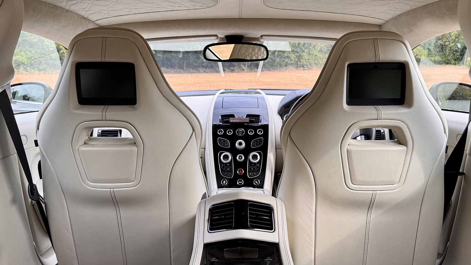 View from the rear cabin of Aston Martin Rapide S showing cream leather front seats with integrated screens and centre console.