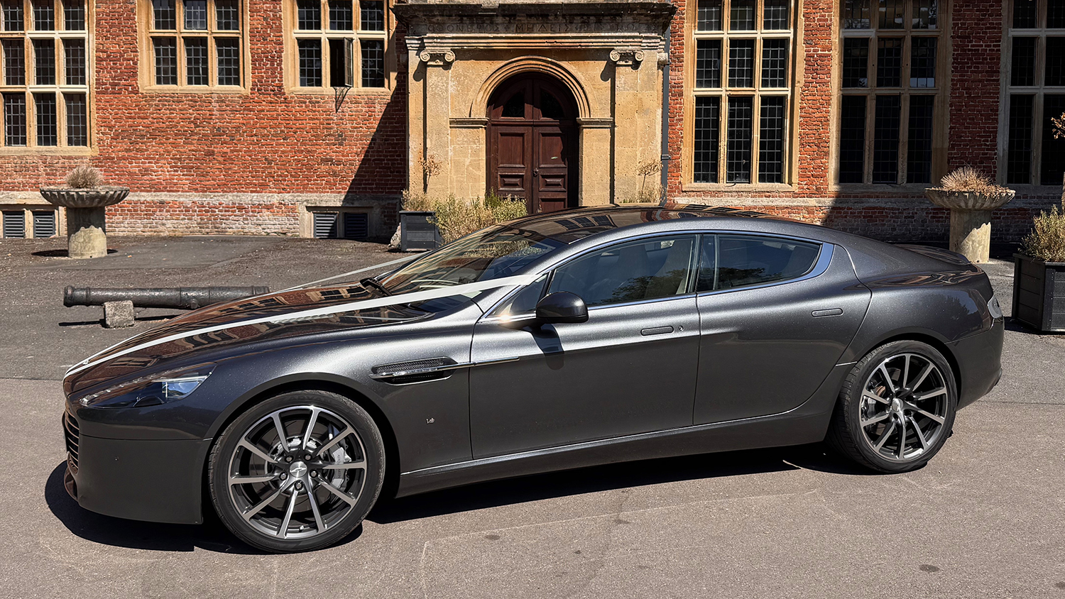 Left side view of metallic silver Aston Martin Rapide S V12 four door luxury sports car outside a wedding venue.