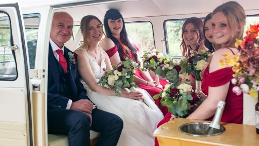 Bride her father and her bridesmaids seating in the rerar compartment of a classic VW Campervan