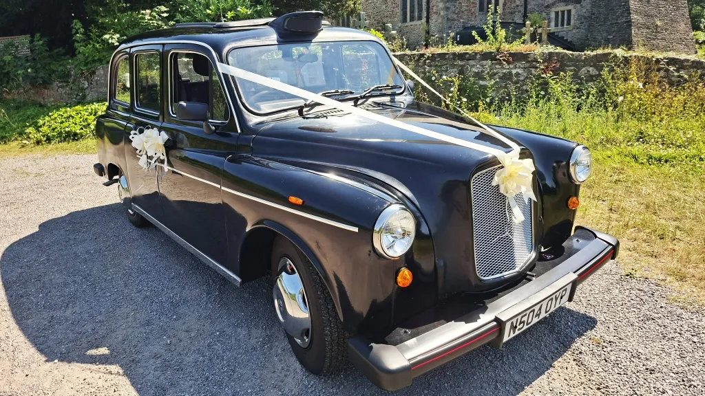 Classic black taxi cab decorated with ivory wedding ribbons and bows outside a church in Barry, South Wales.