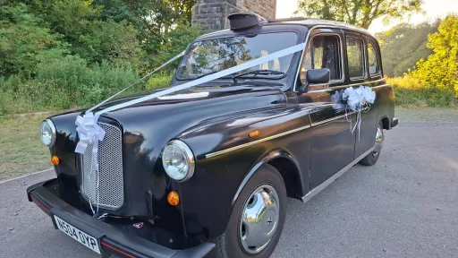 Front left view of classic black taxi cab decorated with ivory wedding ribbons and bows in Barry, South Wales.