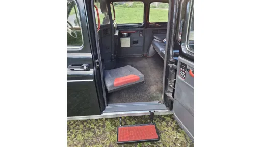 Open rear passenger door of classic black taxi cab showing the wide entrance and access step.
