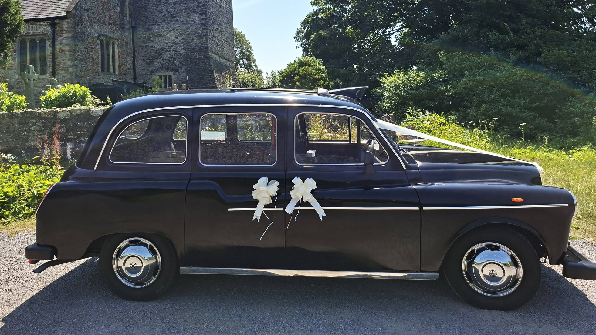 Right side view of classic black taxi cab decorated with large ivory wedding bows in Barry, South Wales.
