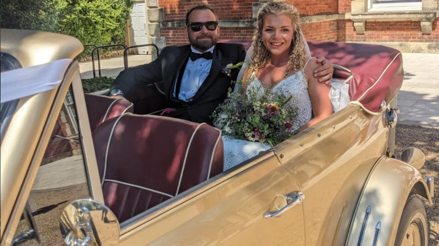 Bride and groom seated inside gold Beauford Convertible showing the burgundy leather interior and open-top cabin.