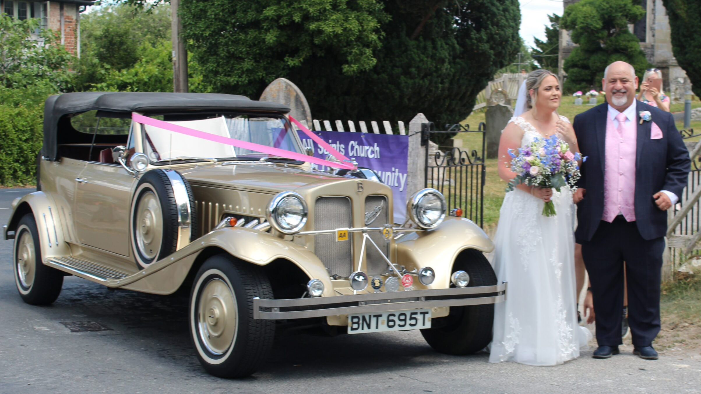Bride and groom standing beside gold Beauford Convertible decorated with wedding ribbons and bows.