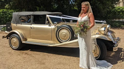 Bride standing beside gold Beauford Convertible with black soft-top roof raised.