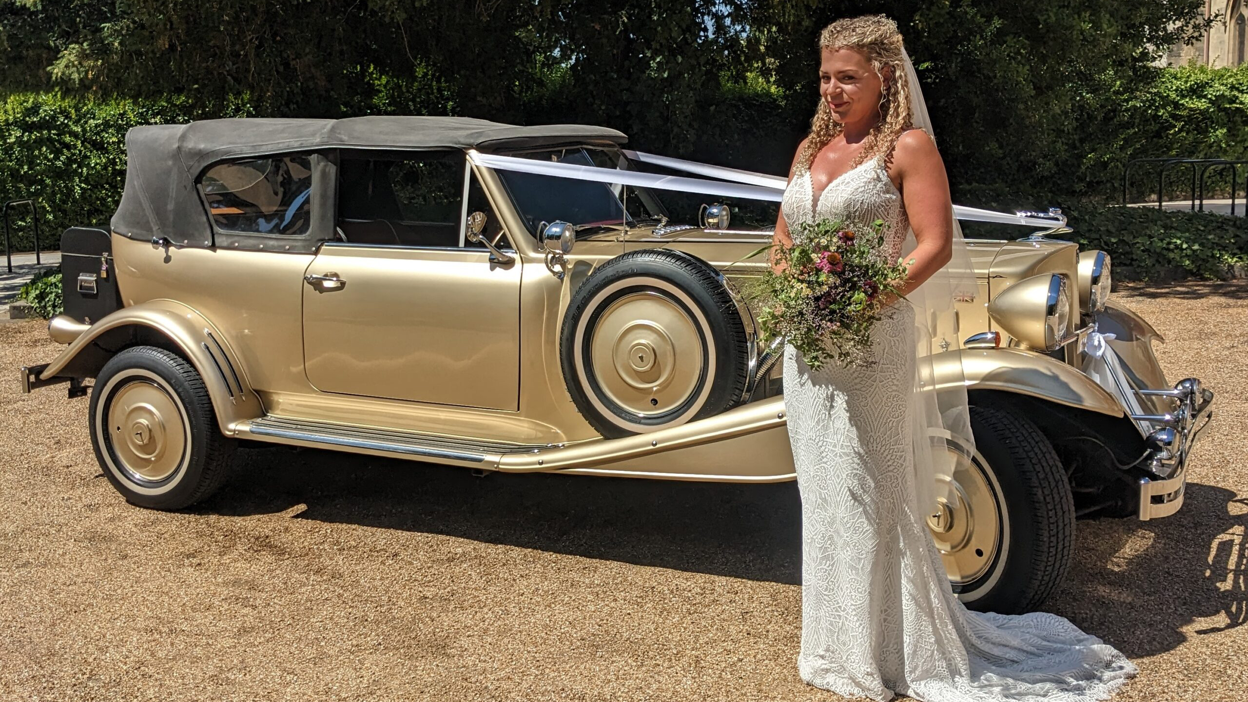 Bride standing beside gold Beauford Convertible with black soft-top roof raised.