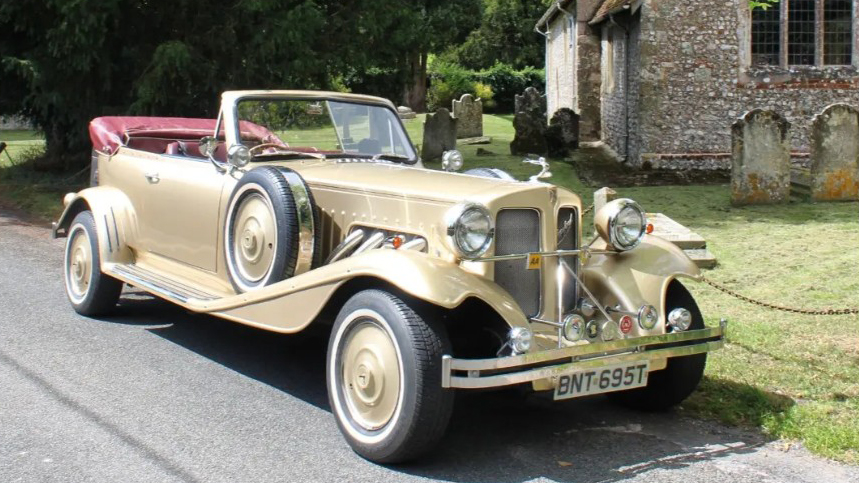 Front three-quarter view of gold Beauford Convertible with burgundy interior, chrome grille and side-mounted spare wheels.
