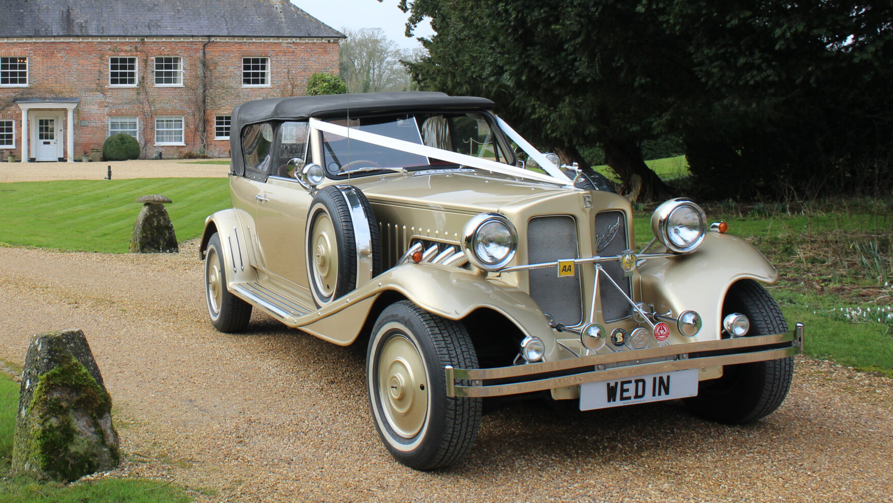 Front three-quarter view of gold Beauford Convertible wedding car parked in the Wiltshire countryside.