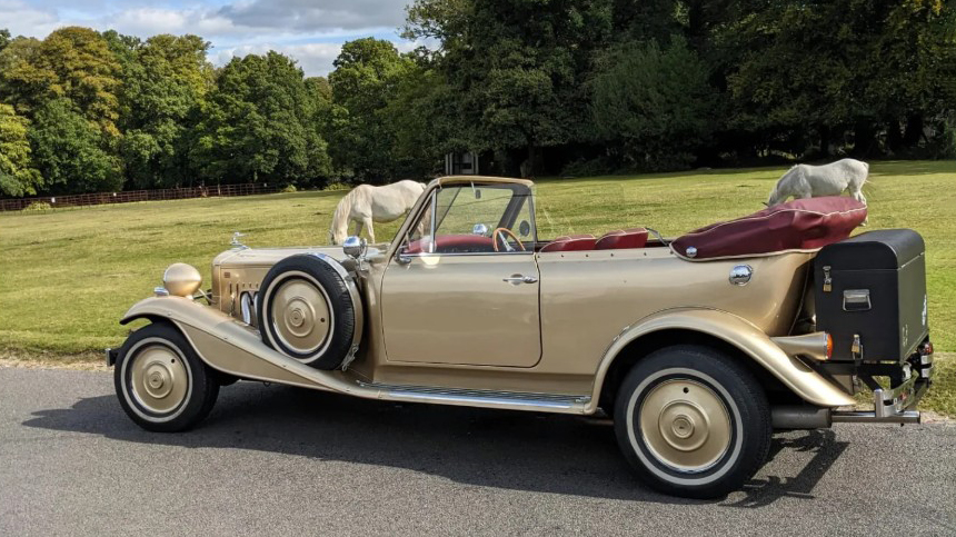 Left side view of gold Beauford Convertible showing its long vintage-style body, side-mounted spare wheel and open roof.