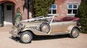 Side view of gold Beauford Convertible with burgundy interior parked outside a country wedding venue in Wiltshire.
