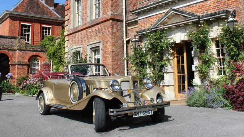 Gold Beauford Convertible decorated for a wedding and parked outside a traditional Wiltshire wedding venue.