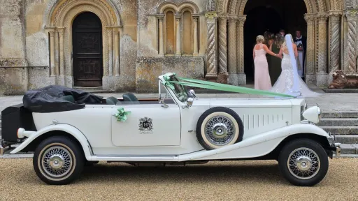 White Beauford Convertible wedding car with dark green interior parked outside a church with the bride in the background entering the Church