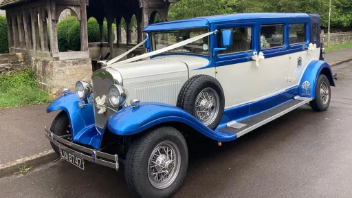 Blue and white Bramwith Landaulette vintage-style wedding car parked outside a church