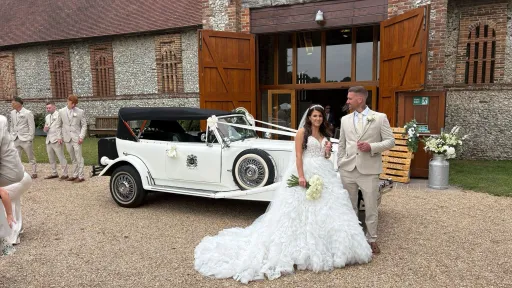Bride and groom standing beside a white Beauford Convertible wedding car with dark green interior at a Hampshire wedding venue