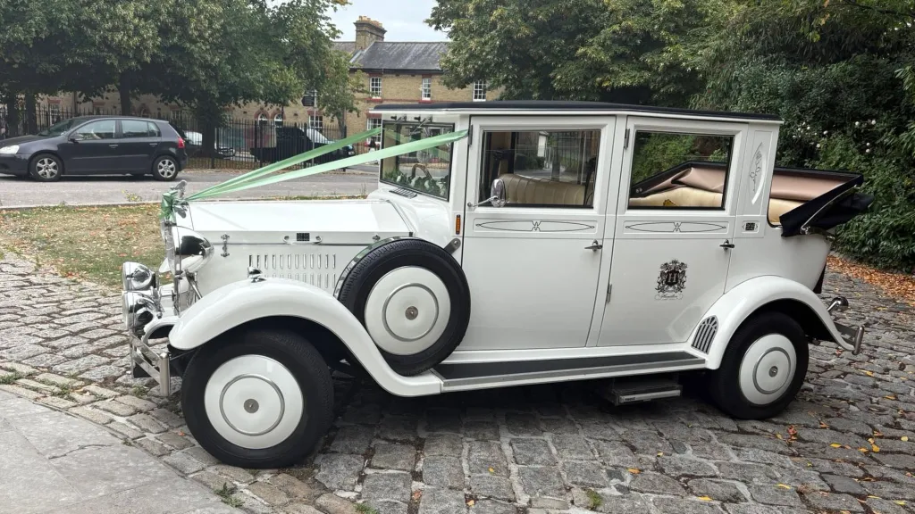 Left side view of the white Imperial Viscount 7-passenger vintage-style wedding car creassed with sage green and ivory ribbons.
