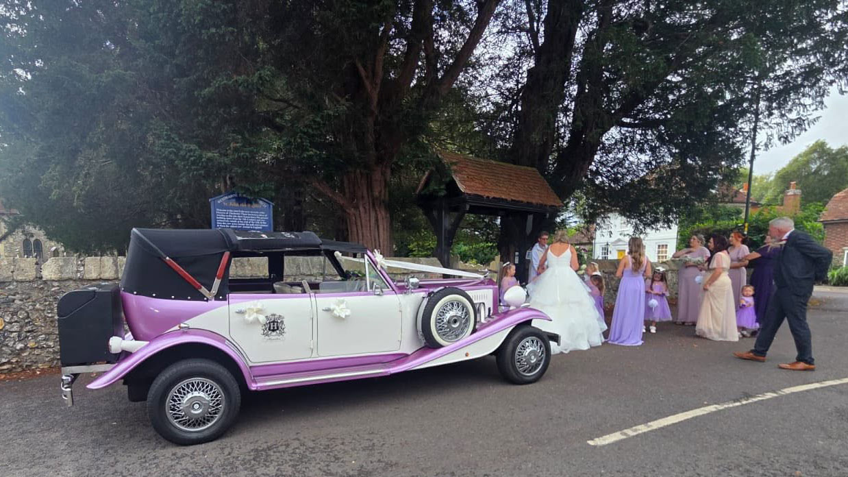 Lilac and white Beauford Convertible wedding car with its roof lowered while on wedding duties
