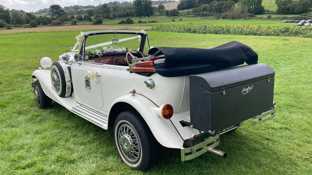 Rear three-quarter view of a white Beauford Convertible with its dark green soft top fully lowered