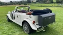 Rear three-quarter view of a white Beauford Convertible with its dark green soft top fully lowered