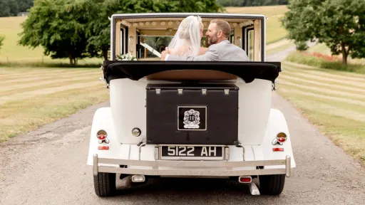 Rear view of the white Imperial Viscount Landaulette with the roof open and wedding couple seated inside