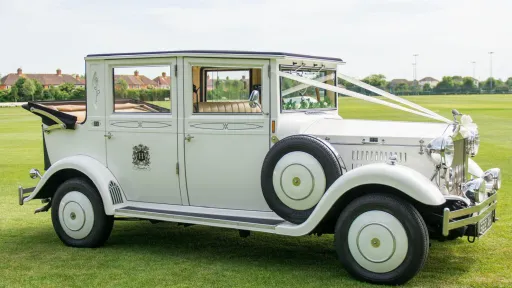 White Imperial Viscount Landaulette 7-passenger wedding car in Hampshire with landaulette roof open, side mnounted spare wheel and Ivory ribbons and bows.