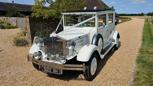 White Imperial Viscount Landaulette with its rear roof open and dressed with Ivory ribbons and bows at a wedding venue