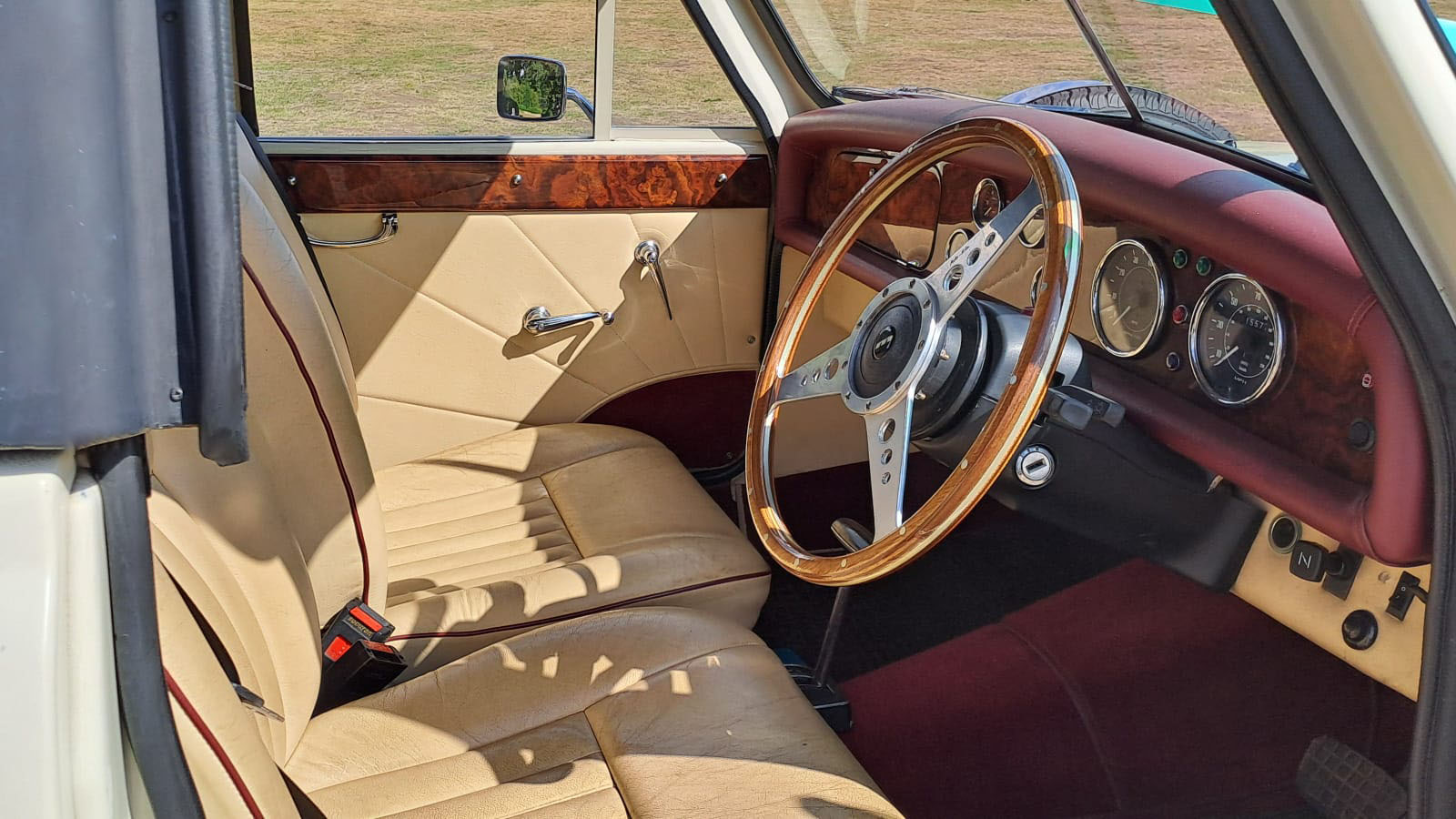 Front driver area of Old English White Beauford Convertible with wood dashboard and cream leather interior