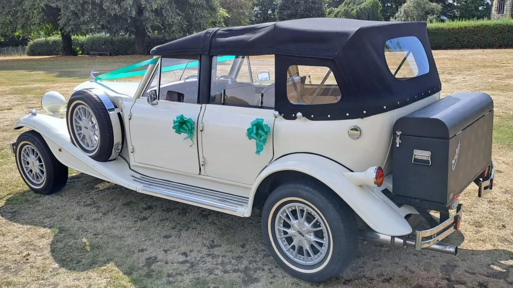 Rear three quarter view of Old English White four door Beauford Convertible with black soft top roof and black picnic trunk at the rear