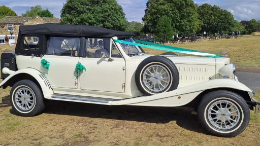 Right side view of Old English White four door Beauford Convertible wedding car with black soft top roof and green ribbons and bows on door handles