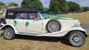 Right side view of Old English White four door Beauford Convertible wedding car with black soft top roof and green ribbons and bows on door handles