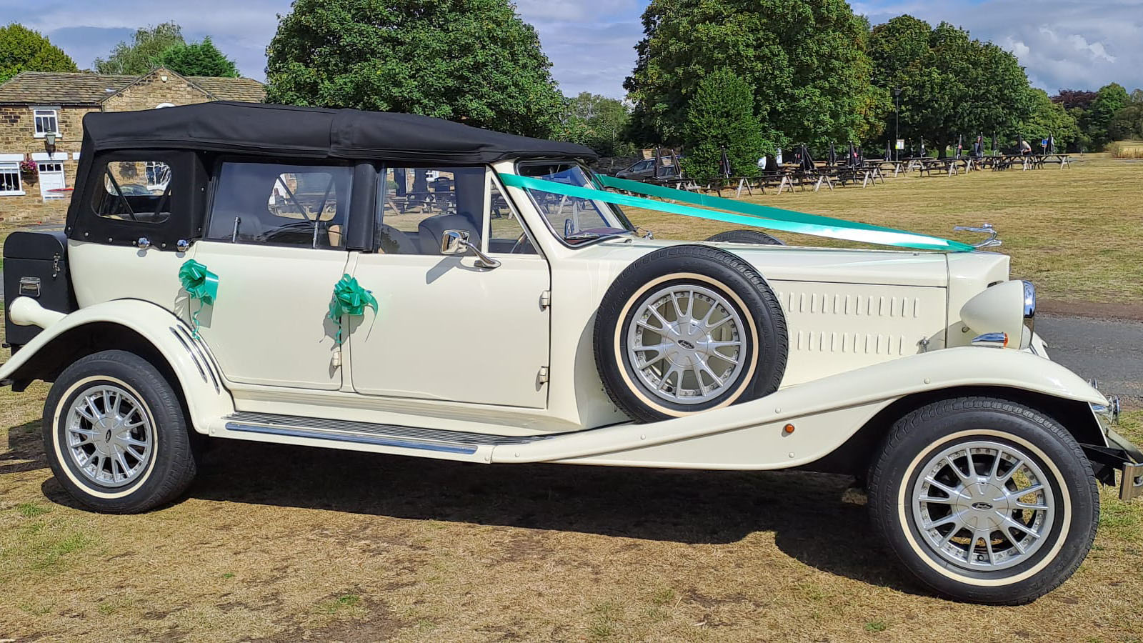 Right side view of Old English White four door Beauford Convertible wedding car with black soft top roof and green ribbons and bows on door handles
