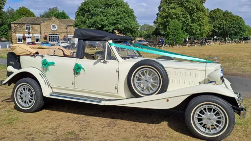Right side view of Old English White four door Beauford Convertible wedding car with roof open and green wedding ribbons and bows, thin white wall tires.