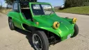 Front side view of a green classic VW beach buggy showing its open doorway and black seats
