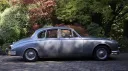 Full side profile of a silver classic Jaguar Mk2 parked beside trees